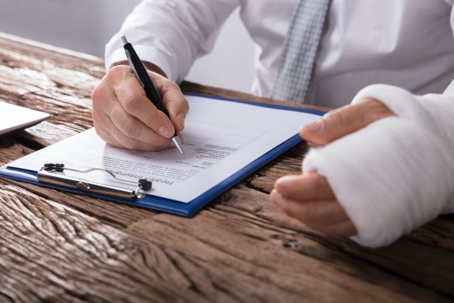 Injured employee filling-up a form on a wooden table.